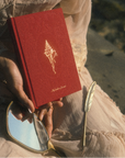 Red journal with gold emblem held by a person on a beach