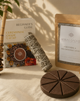 Ceremonial grade cacao products including a book, packaging, and smudge and molinillo on a textured surface.