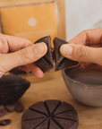 Hands holding two pieces of cacao with a packaging of golden focus on a blurry background on a wooden surface.