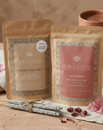 Two packages of Herbal Cacao on a textured surface with flowers and incense sticks.