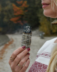 Woman holding a smudge stick in her hand with trees in the background