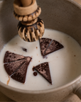 Cacao pieces being added to a pan of milk to whisk with a molinillo traditional cacao whisk