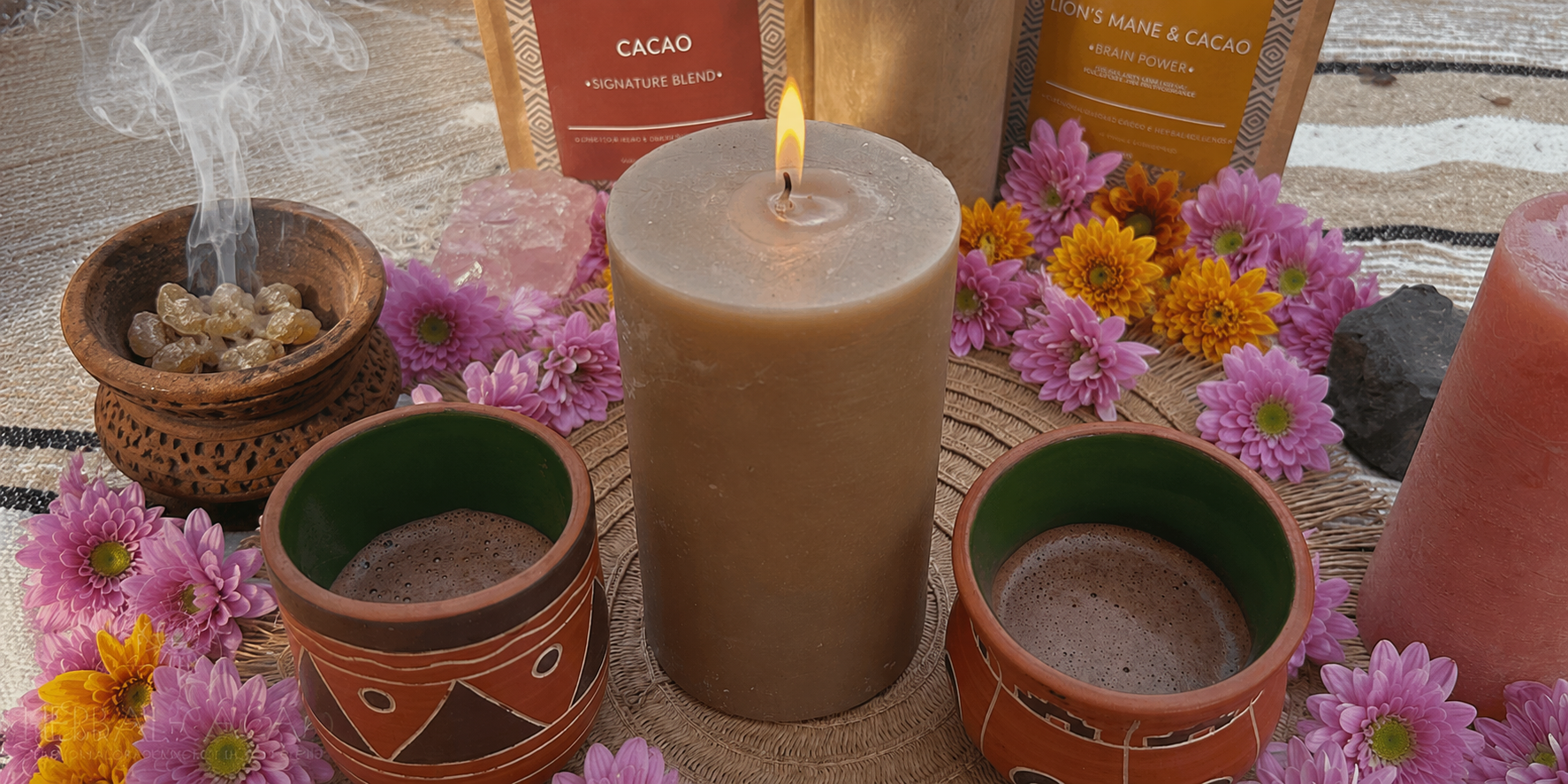 Ceremonial cacao, candle and incense setup with flowers and Herbal Cacao packaging on a textured surface