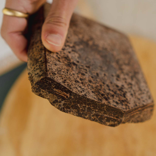 Close-up of a hand holding a ceremonial cacao block against a blurred background