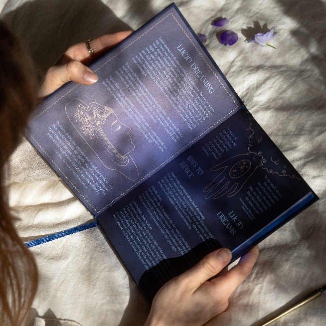 Person holding an dream journal with mystical designs and text on a textured surface.
