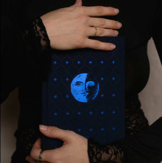 Dream Journal with a sark blue embroidered book with a moon and star design held by hands.