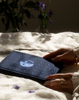 Person holding a dream journal with a white design on a textured surface with flowers.