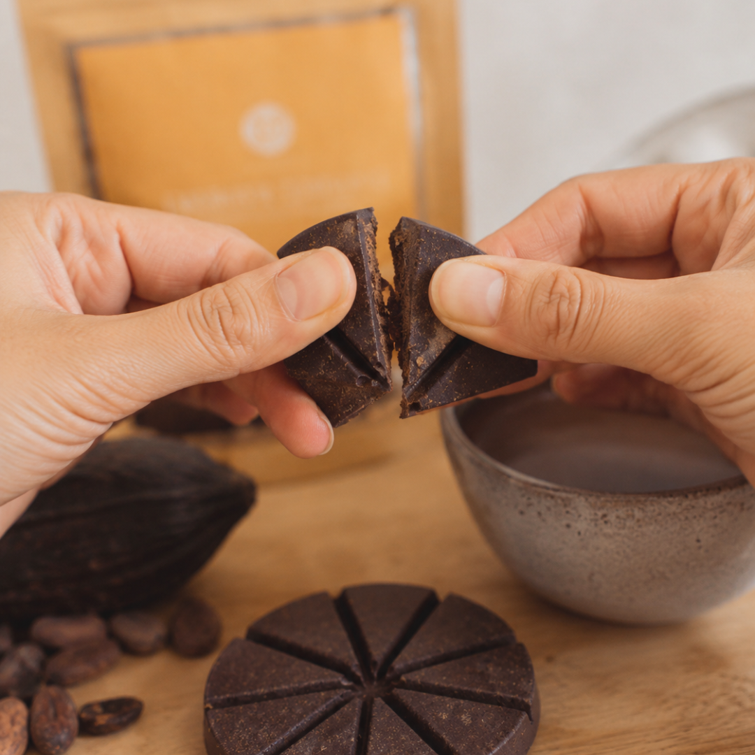 Hands holding two pieces of cacao with a packaging of golden focus on a blurry background on a wooden surface.