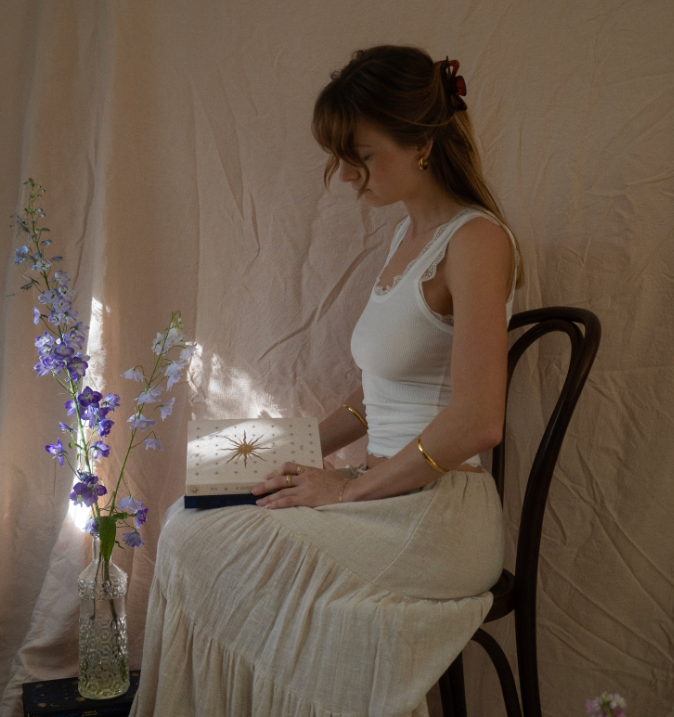 Woman sitting on a chair with a Gratitude Journal, wearing a white dress in a softly lit room.