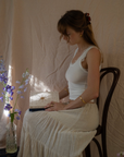 Woman sitting on a chair with a Gratitude Journal, wearing a white dress in a softly lit room.