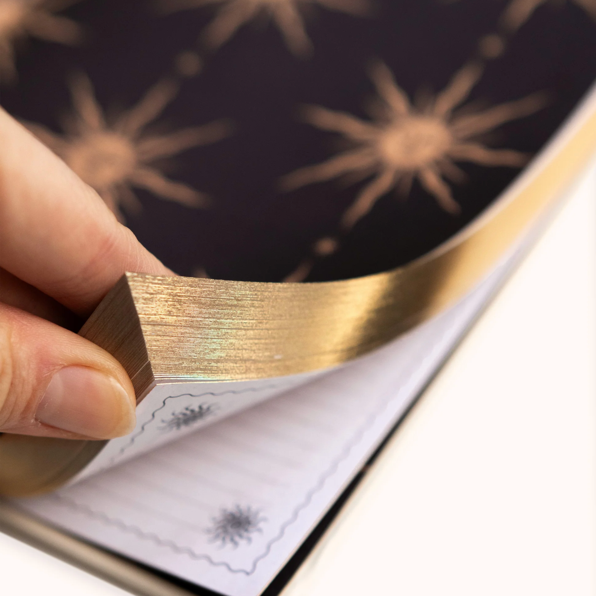 Hand holding a gold Gratitude Journal over a black surface with star-like patterns
