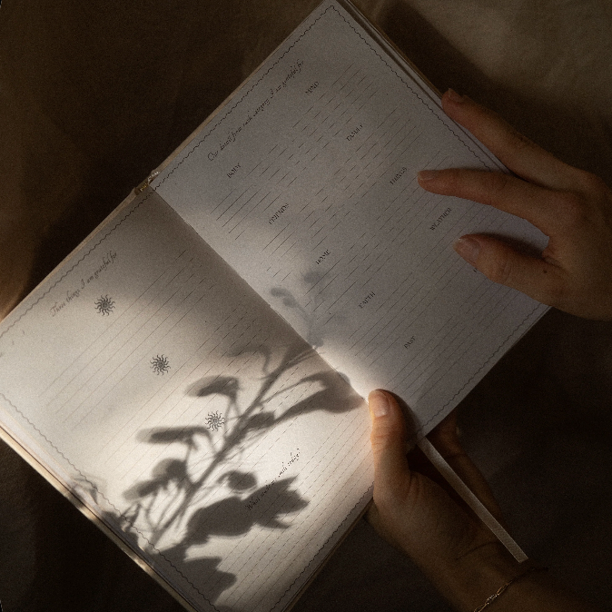 Open GratitudeJournal with plant shadows on a dark surface