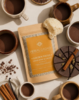 Packaging of Herbal Cacao Golden Focus with mugs of cacao, lionsmane, cinnamon and vanilla beans on a light background