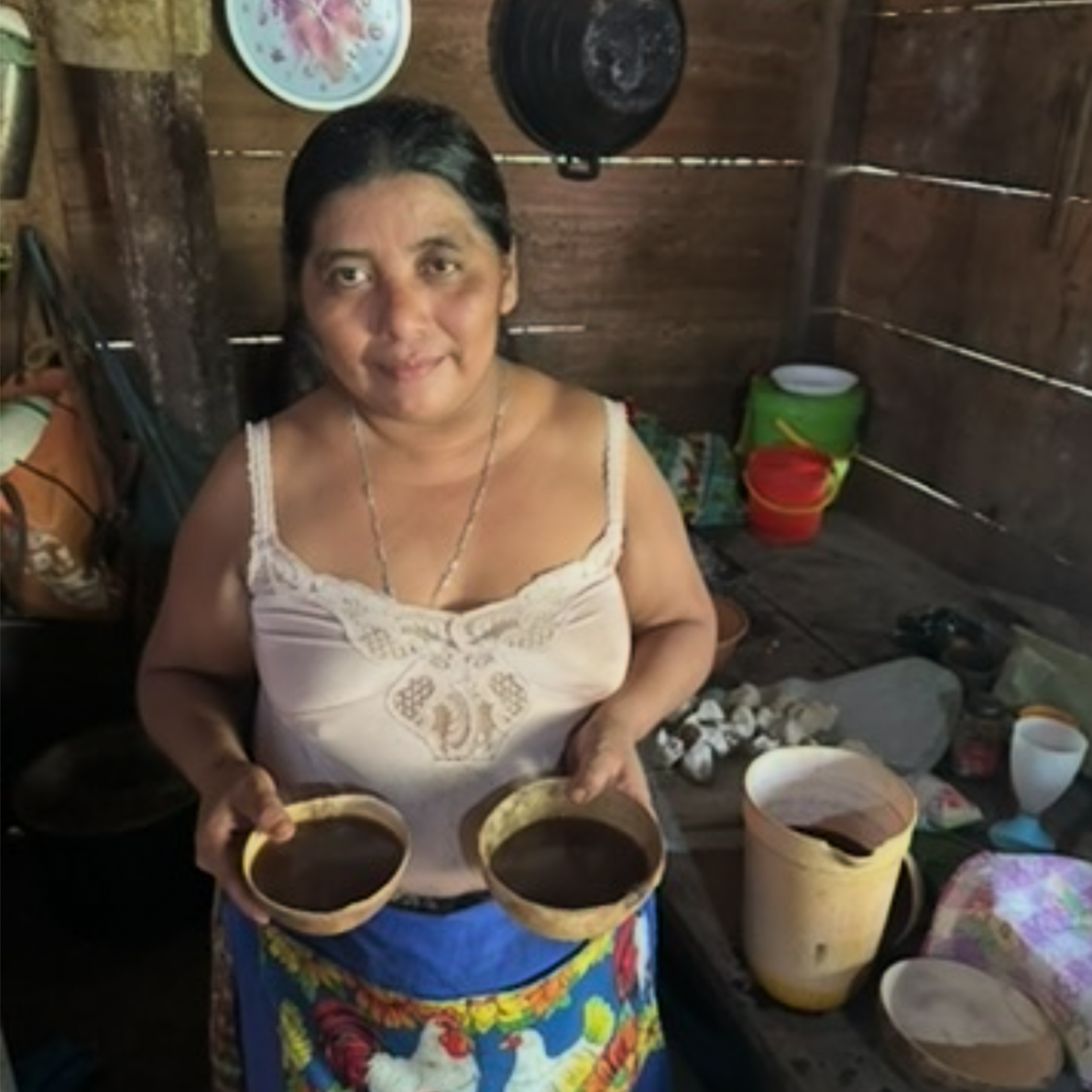 Woman holding two bowls of cacao in a kitchen setting with various items on the counter.