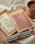 Herbal Cacao products including packets, a cup of cacao, and incense sticks on a textured surface.