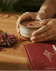 Person holding a mug of cacao with Herbal Cacao packaging and ingredients on a wooden table.