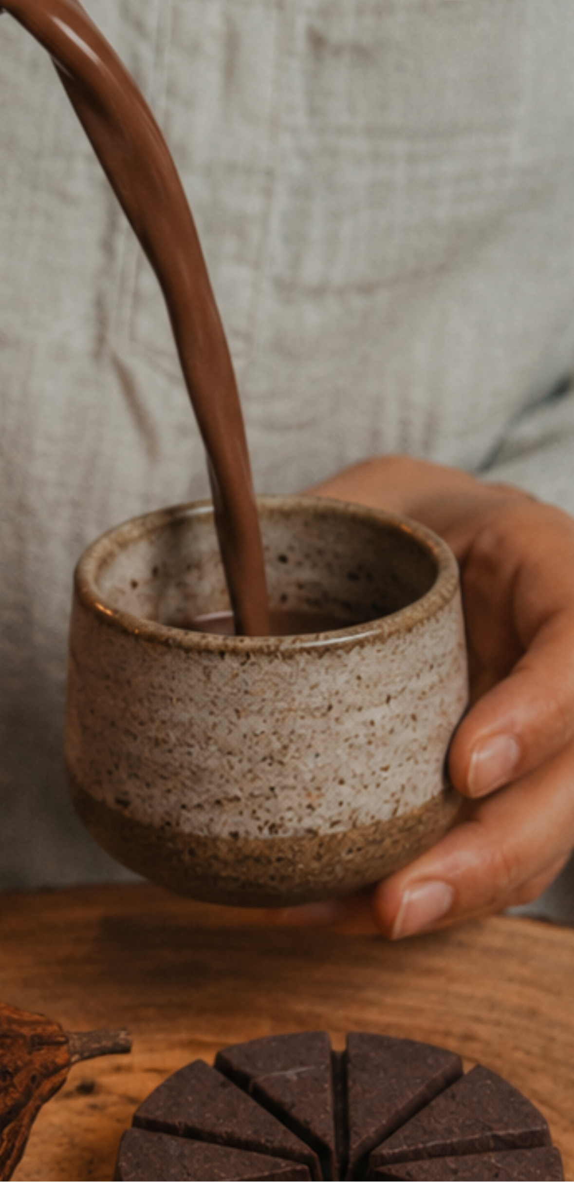 Hand pouring a cacao into a ceramic cup on a wooden surface.