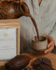 Person pouring cacao into a cup with a bag of Herbal Cacao in the background.