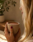 Sharon holding a cup of cacao with both hands and with a plant in the background