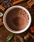 Signature Blend Ceremonial Cacao from Herbal cacao in a mug surrounded by cinnamon sticks, cacao beans, and other spices on a wooden surface.