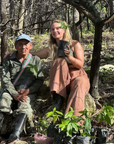 Two people sitting in a burned down cacao forest, with baby cacao tree