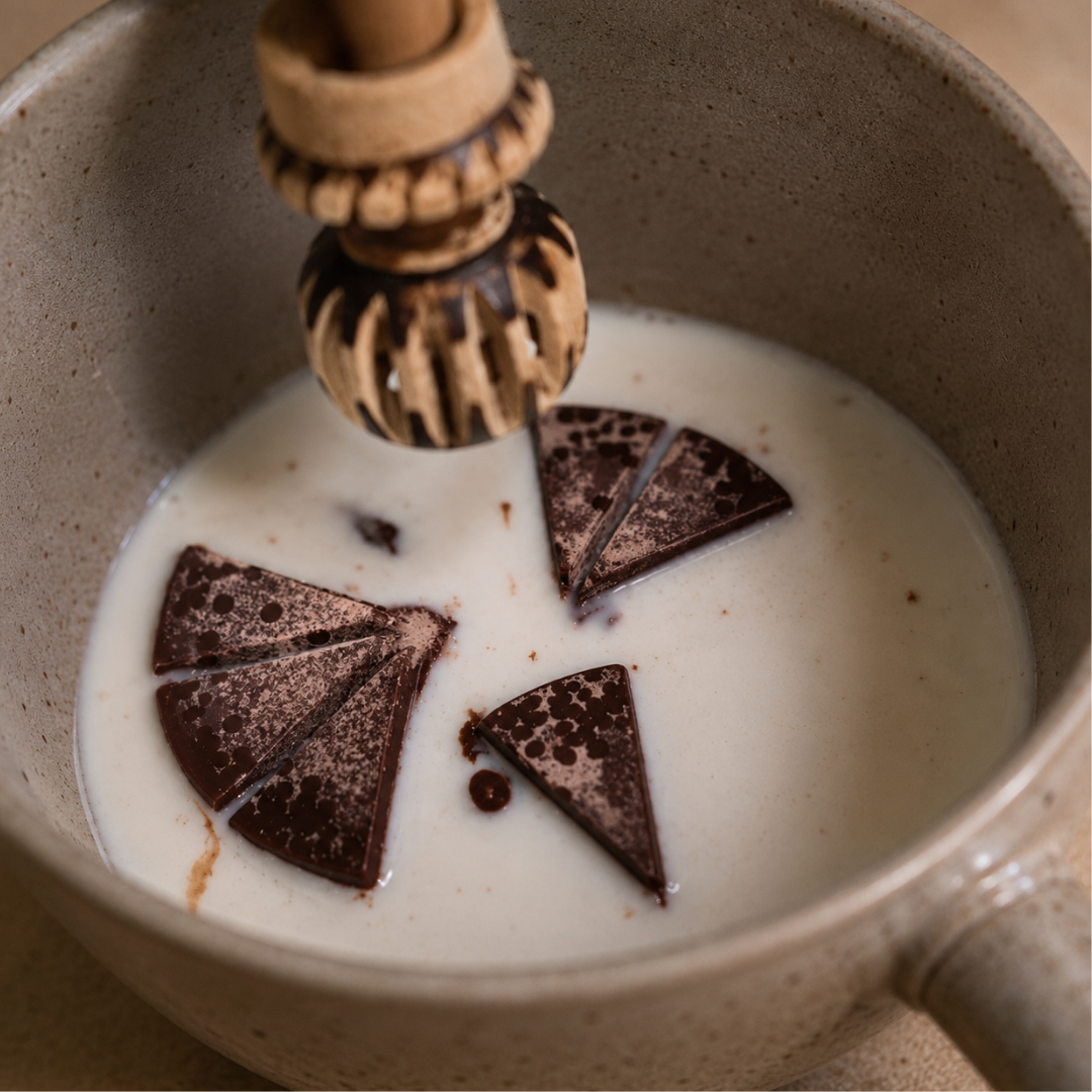 Cacao pieces being added to a pan of milk to whisk with a molinillo traditional cacao whisk